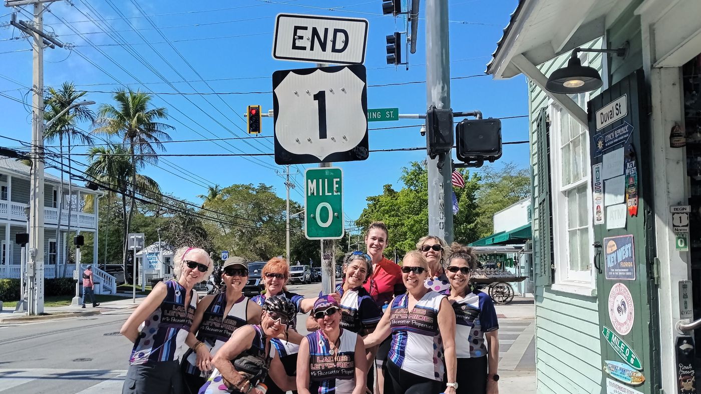A group of riders celebrating under the End US 1 and Mile 0 signs in Key West