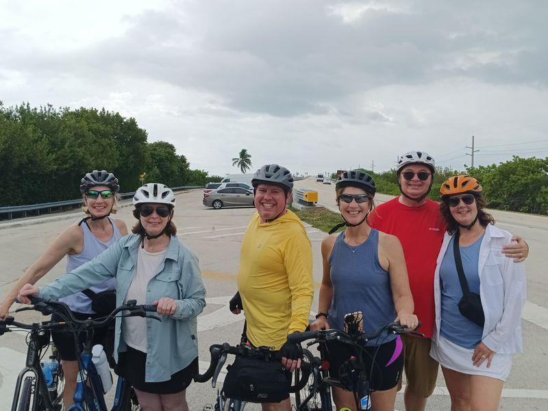 Six smiling riders in helmets stopped at a bridge in the Keys